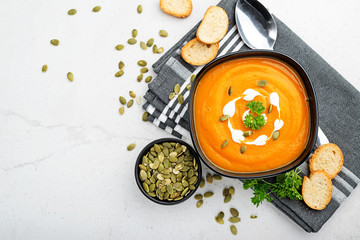 Pumpkin and carrot soup with cream and parsley on gray background. Top view