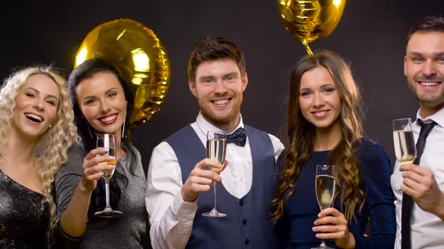 celebration, luxury and holidays concept - happy friends with golden balloons and champagne glasses at party over black background