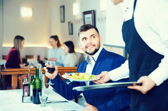 Waiter serving delicious salads to handsome young man at restaurant