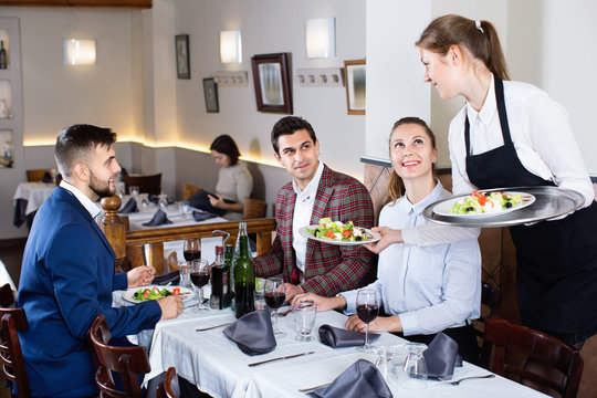 Polite smiling waitress bringing ordered dishes to guests at restaurant