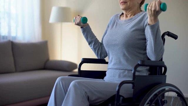 Senior woman in wheelchair lifting dumbbells, doing exercises at home, recovery