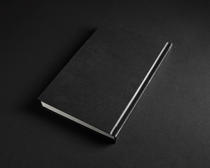 Blank black hardcover book on black paper background.
