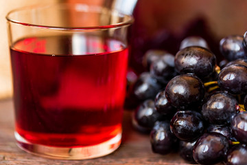 Red grape juice in glass and grapes close