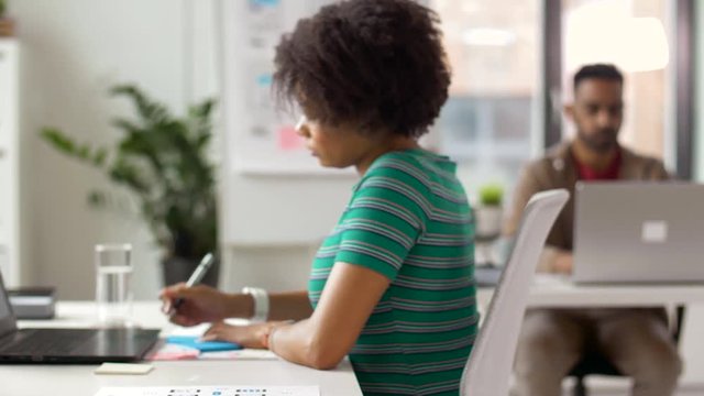 business and creative people concept - office workers with laptop computers taking notes