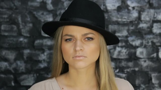 Portrait of a blonde in a black hat against a brick wall background