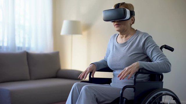 Aged female sitting in wheelchair and wearing virtual reality headset, game
