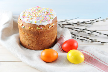 Easter cake on cloth napkin. Around the chicken eggs are red, yellow and orange. In the frame of the willow branch. Light wooden background. Close-up.