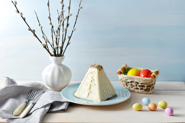 Curd Easter dessert pasha. The dessert is decorated with sweets in the form of eggs. In the background is a figure of a rabbit and a vase with a willow. Light background. Close-up. Macro photography.