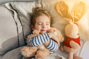 Beautiful baby girl sleeping in my own bed at home with a favorite toy bear.	