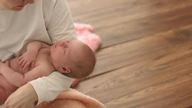 Happy mother looks at her naked sleeping newborn baby with love