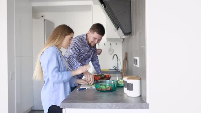 A young woman and her adult man fool around and laugh in their new kitchen while cooking vegetable salad