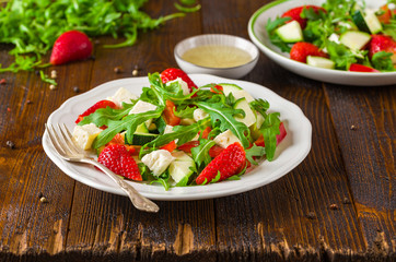 Fresh vegetable strawberry salad on white plate on natural rustic desk.