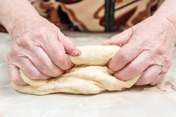 Obraz na płótnie Canvas Hands of an elderly woman knead the dough on a table, close-up