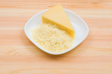 Close-up on a wooden table in a plate is Parmesan cheese in grated and brick form. The concept of solid dairy products