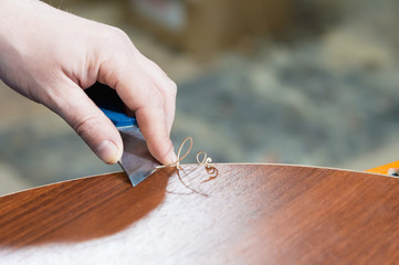 A close-up of the real male carpenter's not well-groomed hands completes the finish of the chipboard details of the furniture by cutting off the edge of the edge of the stripped decorative strip. The