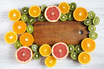 Flat lay. Top view. Wooden board in the center with sliced kiwi, orange, grapefruit and mandarin on light background. Summer background