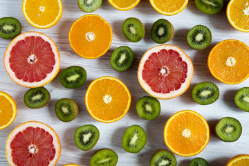 Flat lay. Top view. Sliced tropical fruits: kiwi, orange, grapefruit and mandarin on light wooden background. Summer background