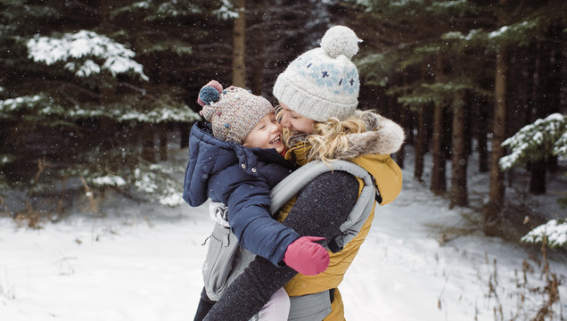 Cheerful mother carrying daughter in forest during winter