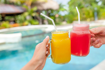 Two colorful fruit shakes in hands. Summer and tropical mood. Cold blended drinks, mango and watermelon fruit smoothie. Clink glasses by couple hands