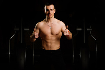 Smiling handsome young sportsman showing thumbs up. Portrait of strong healthy handsome Athletic Man Fitness Model at a gym
