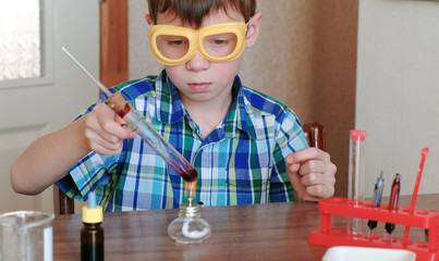 Experiments on chemistry at home. Boy heats the test tube with red liquid on burning alcohol lamp. The liquid boils.