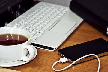 A cup of hot tea on the table next to the laptop and phone