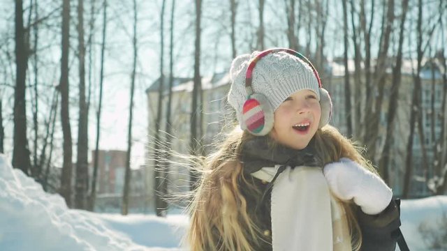 little funny girl with headphones on her head and Teddy bear with her hand running through the winter Park, smiling and spinning. The street is beautiful Sunny, frosty weather. Steadicam shot