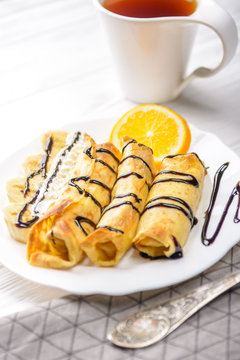 Pancakes with banana, whipped cream decorated with chocolate syrup on white wooden background. And a cup of tea