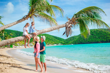 Little girls having fun sitting on the palm tree. Happy family relaxing on tropical beach with white sand and turquoise ocean water