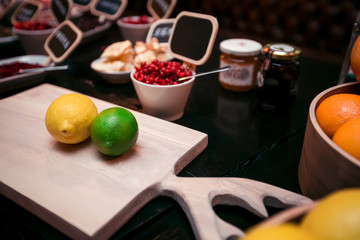 Ingredients for homemade alcoholic tincture: lime, lemon, oranges, cranberries, rose petals on a wooden cutting board with antlers