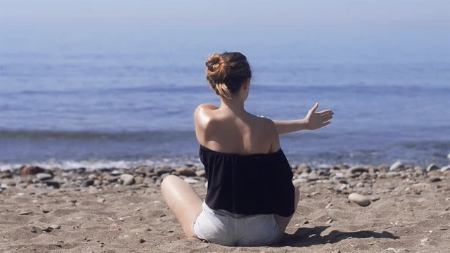 Young woman makes meditation in lotus pose on sea / ocean beach, harmony and contemplation. Beautiful girl practicing yoga at sea resort at her vacation. Life style. Young woman relaxing outdoors.