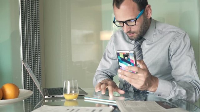 Young businessman working with smartphone and tablet sitting by table at home
