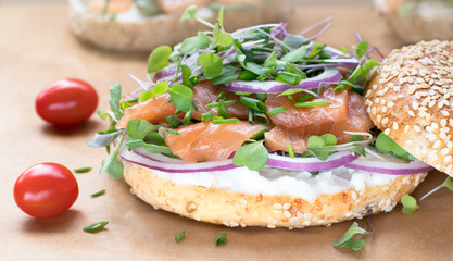 Bagel sandwich with creame cheese, salmon,onion,tomato,greens,chives close-up on a wooden background.