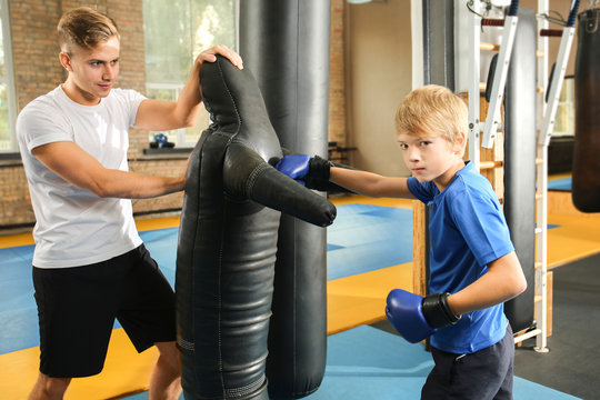 Little boy with trainer near punching dummy in gym