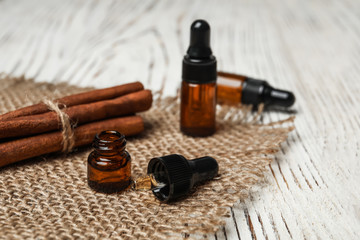 Bottles with cinnamon oil and sticks on wooden table