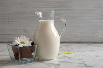 Jug with milk and chocolate pieces on table