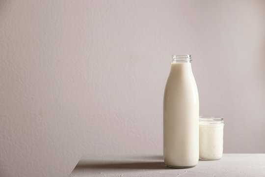 Bottle and glass with milk on table against grey wall