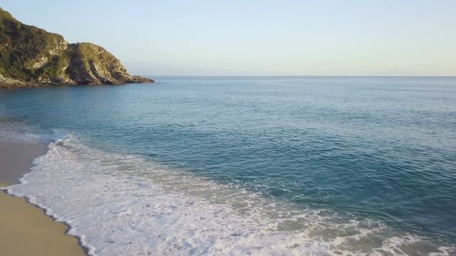 Costa sabbiosa del mare calmo vicino a costa frastagliata con scogli al pomeriggio vicino al tramonto 