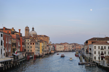 Grand Canal of Venice at dusk with full moon glowing overhead with clear blue sky.