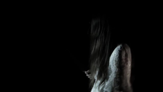 A little ghost girl with long black hair, in white, wandering through the woods with a knife and a soft toy. 4k