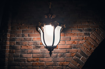 Big large forged vintage sconce lamp on a brick orange wall at night in the dark