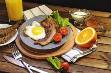English Breakfast: fried egg with bacon, orange juice, tomatoes, zernovoi bread, lettuce leaf, top view.