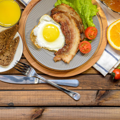 English Breakfast: fried egg with bacon, orange juice, tomatoes, zernovoi bread, lettuce leaf, top view.