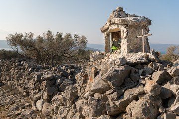 Small white chapel and a metal cross on a stone wall near Cres