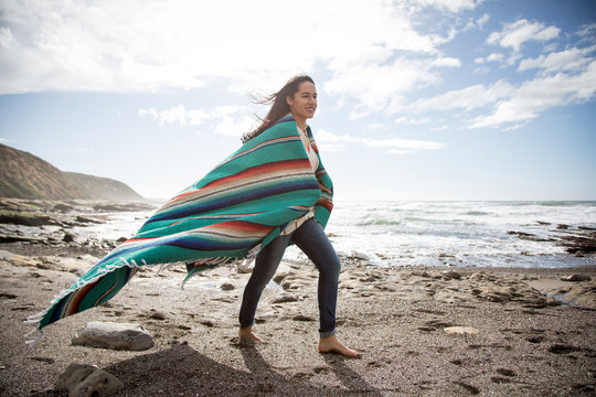 Woman wraps up in a blanket at the beach.