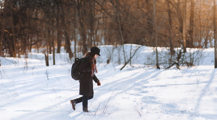 A girl with a backpack in the winter forest walks through the snow. Walk alone in frosty weather. Snowdrift.