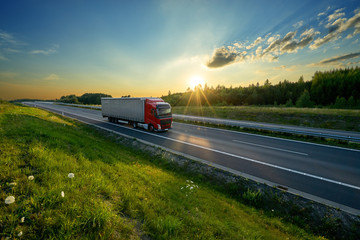 Red truck driving on the highway in the countryside in the rays of the sunset
