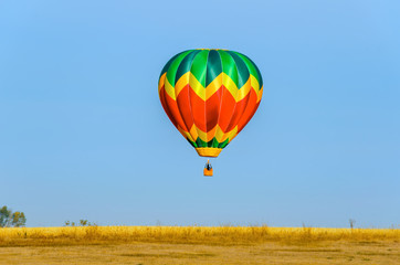 Fototapeta premium multi-colored balloon with a basket, a flame of fire takes off into the blue sky