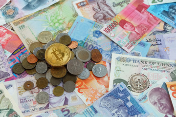 Gold bitcoin coin on top over international traditional coins and banknotes
