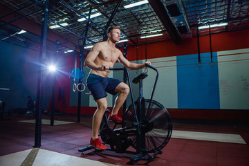 Obraz na płótnie Canvas Fit young man using exercise bike at the gym. Fitness male using air bike for cardio workout at cross training gym.